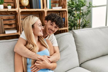 Kanepede oturan genç çift evde sarılıyorlar..