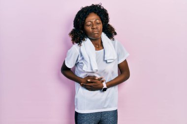 Afro-Amerikalı genç bir kadın spor giyer ve havluyu midesine indirir çünkü hazımsızlık, acı veren hastalıklar kendini iyi hissetmez. Ağrı kavramı. 