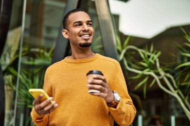 Genç Afrikalı Amerikalı adam akıllı telefon kullanıyor. Şehirde kahve içiyor..