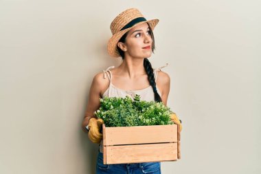 Genç İspanyol kadın elinde yeşil saksı tutarken gülümsüyor, yan tarafa bakıyor ve düşünüyor.. 