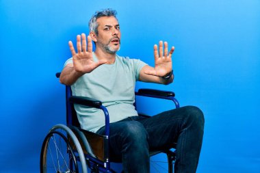 Yakışıklı, orta yaşlı, gri saçlı, tekerlekli sandalyede oturan, avuç içi hareketlerini durduran, sinirli ve hayal kırıklığına uğramış bir adam. 