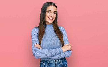 Kış süveteri giyen, kollarını kavuşturup kameraya bakarken gülümseyen genç ve güzel bir kadın. pozitif kişi. 