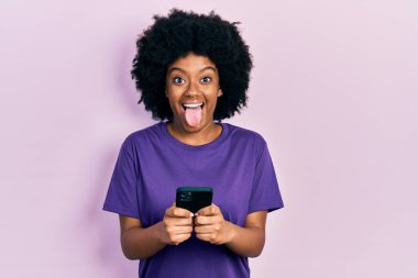 Genç Afrikalı Amerikalı kadın akıllı telefon kullanıyor. Dilini mutlu bir ifadeyle dışarı çıkartıyor.. 