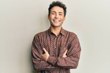 Yakışıklı, sıradan kıyafetler giyen mutlu yüzlü, kollarını kavuşturup kameraya bakan bir İspanyol. pozitif kişi. 