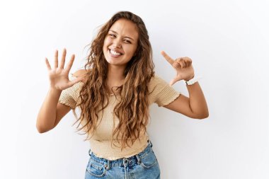 Güzel İspanyol kadın tek başına ayakta dikilirken arka plan 7 numaralı parmaklarını gösterip işaret ederken kendine güvenen ve mutlu bir şekilde gülümsüyor.. 