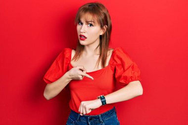 Kırmızı tişörtlü kızıl saçlı genç bir kadın acele ederek saati, sabırsızlığı ve gecikmeyi gösteriyor. 