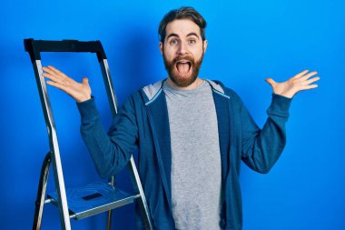 Sakallı beyaz bir adam zaferi kutluyor mutlu bir gülümsemeyle ve ellerini kaldırarak kazanan bir ifadeyle. 