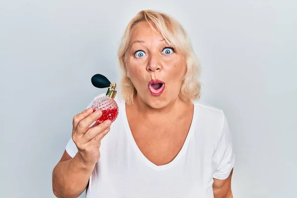 Middle Age Blonde Woman Holding Perfume Scared Amazed Open Mouth — Stock Photo, Image