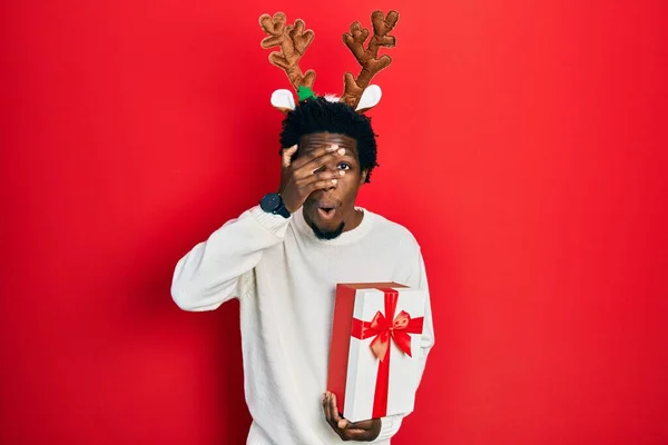 Jovem Afro Americano Vestindo Chapéu Natal Veado Segurando Presente Espreitando — Fotografia de Stock