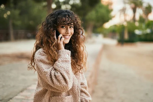 Genç İspanyol kadın gülümsüyor. Parktaki akıllı telefondan konuşarak mutlu oluyor..