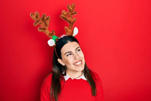 かわいいクリスマストナカイの角を顔に笑顔で横に離れて見て身に着けている若いヒスパニック系の女性は 自然な表情 自信を持って — ストック写真