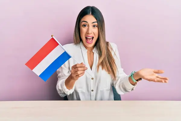 Молодая Латиноамериканка Флагом Голландии Сидящая Столе Празднуя Достижение Счастливой Улыбкой — стоковое фото