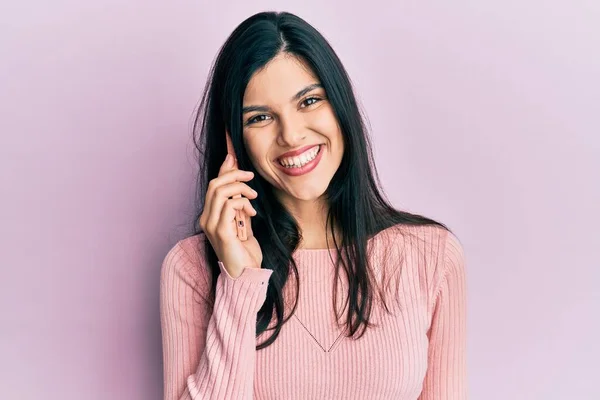 スマートフォンで会話をしている若いヒスパニック系の女性は 前向きな笑顔で笑顔で立って笑顔で歯を見せています — ストック写真