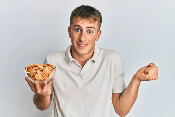 Jovem Caucasiano Segurando Tigela Biscoitos Salgados Gritando Orgulhoso Celebrando Vitória — Fotografia de Stock