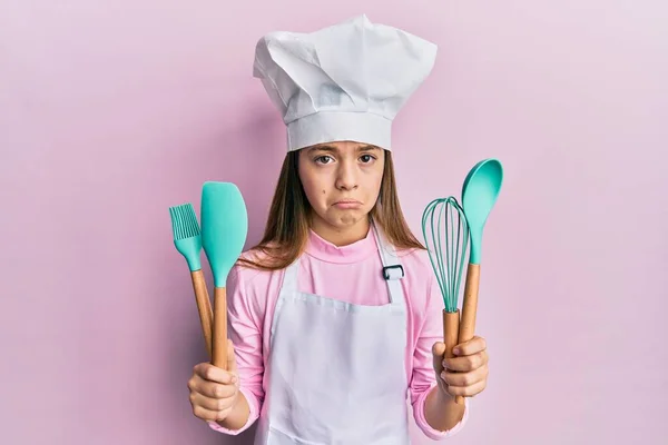 美しいブルネットの女の子は プロの料理エプロンを身に着けている調理器具を落ち込んで 苦痛のために心配し 怒って恐れて泣いています 悲しい表情 — ストック写真