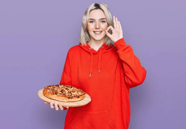 Menina Loira Jovem Segurando Pizza Italiana Fazendo Sinal Com Dedos — Fotografia de Stock