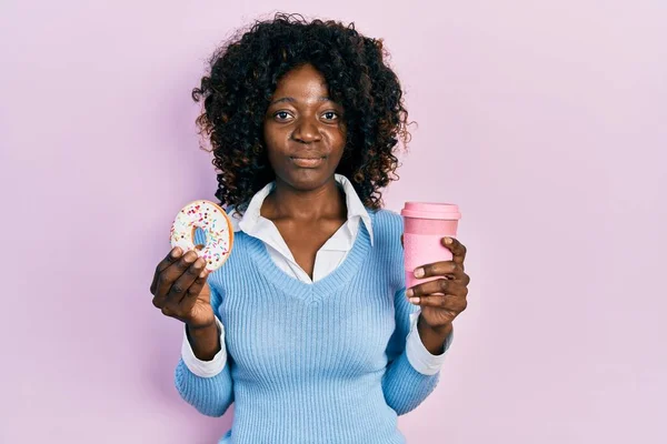 Młoda Afroamerykanka Jedząca Pączki Pijąca Kawę Zrelaksowana Poważnym Wyrazem Twarzy — Zdjęcie stockowe