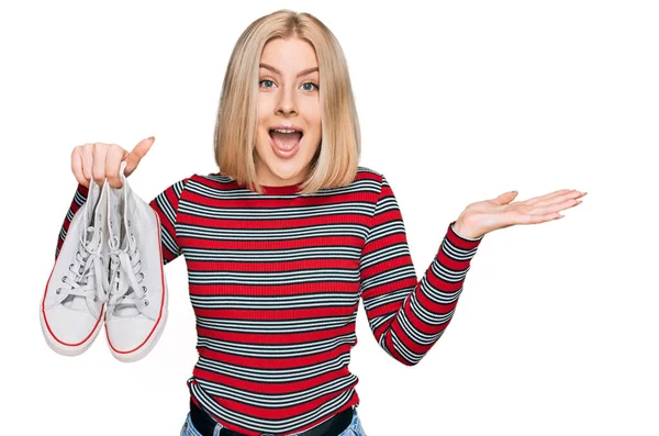 Молода Блондинка Тримає Біле Казуальне Взуття Святкуючи Перемогу Щасливою Посмішкою — стокове фото