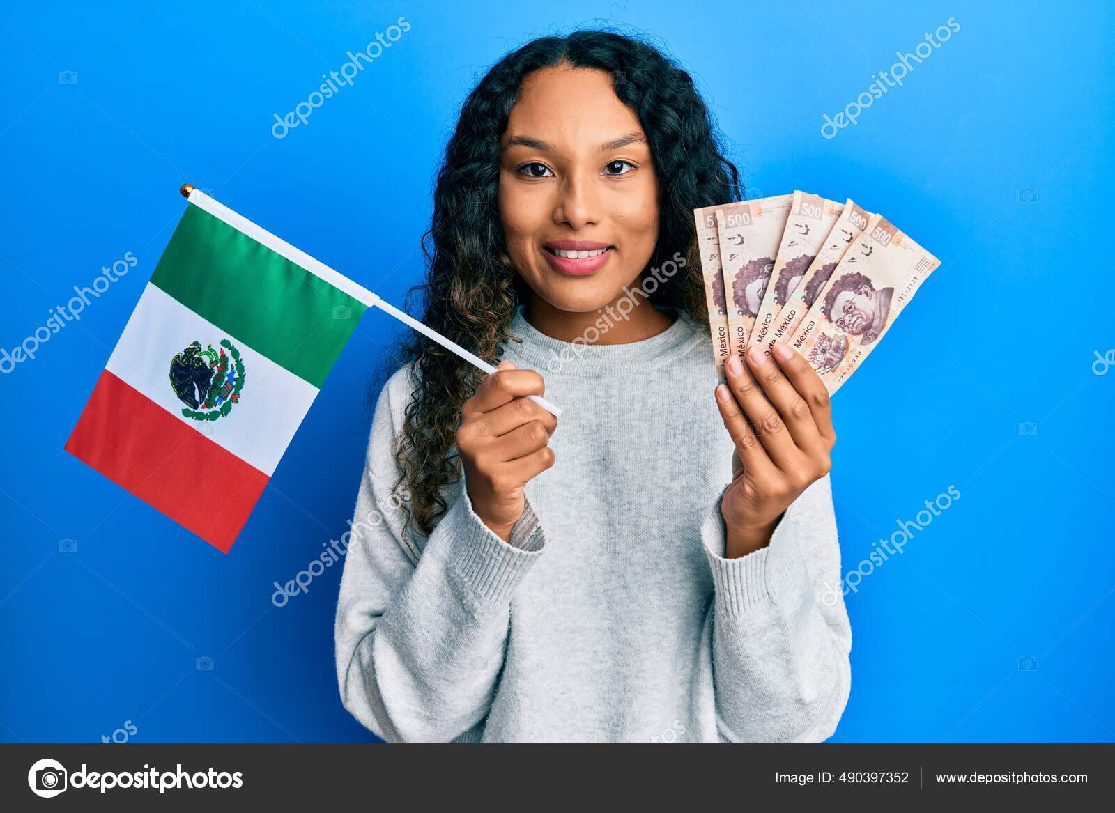 年轻的拉丁女人拿着墨西哥国旗和墨西哥比索钞票脸上挂着快乐而冷静的微笑显示牙齿——图库图片© Krakenimages.com #490397352
