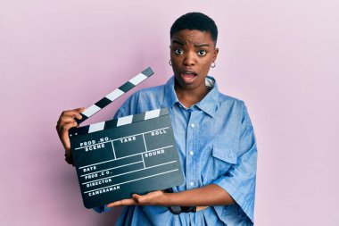 Genç Afro-Amerikalı kadın şok olmuş suratıyla video film panosu tutuyor. Şüpheci ve alaycı bakıyor, ağzı açık kalmış. 