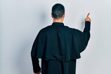 Sakallı, Katolik rahip cüppeli yakışıklı bir adam tersten öne doğru poz veriyor. 