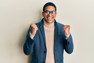 Zarif kıyafetler ve gözlük takan yakışıklı İspanyol adam kollarını kaldırarak ve açık gözlerle başarıyı kutluyor ve şaşırıyor. Kazanan konsept. 