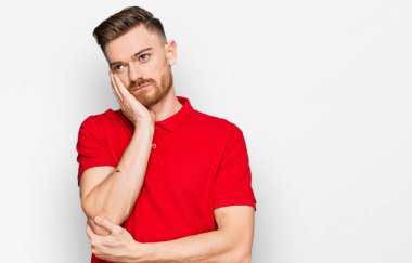 Genç kızıl saçlı, günlük kıyafetler giyen, kollarını kavuşturarak depresyondan sıkılmış ve yorgun gözüken bir adam.. 