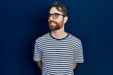Sakallı, çizgili tişörtlü ve gözlüklü beyaz bir adam yüzünde gülümseme, doğal bir ifade. Kendinden emin gülen. 