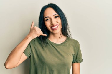 Sıradan tişörtler giyen, gülümseyen, el ve parmaklarıyla telefon hareketi yapan, telefonda konuşan İspanyol bir kız. iletişim kavramları. 