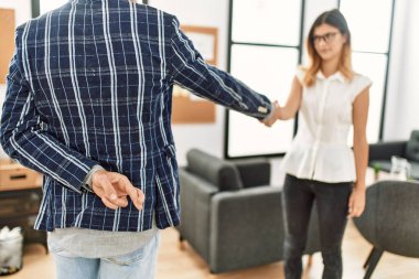 İki iş adamı mutlu bir şekilde el sıkışırken gülümsüyor. Ofiste şans dileyerek duran bir adam..