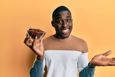 Genç Afrikalı Amerikalı adam elinde kuru üzümlü bir kâseyle başarıyı mutlu bir gülümsemeyle kutluyor ve kazanan el kaldırarak ifade ediyor. 