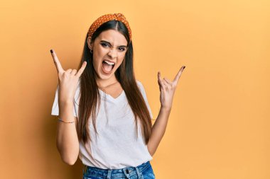 Güzel esmer, beyaz tişört giyen, çılgın bir ifadeyle bağıran ellerini kaldırarak rock sembolü yapan genç bir kadın. Müzik yıldızı. ağır kavram. 