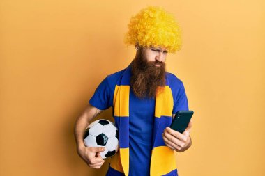 Kızıl saçlı, uzun sakallı futbol holiganı amigoluk oyunu elinde akıllı telefon tutarak depresif ve endişeli, sinirli ve korkmuş bir şekilde ağlayan bir adam. hüzünlü ifade. 