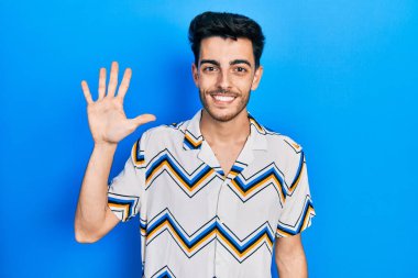 Gündelik kıyafetler giyen genç İspanyol adam beş numarayı gösterip işaret ederken kendinden emin ve mutlu bir şekilde gülümsüyor.. 