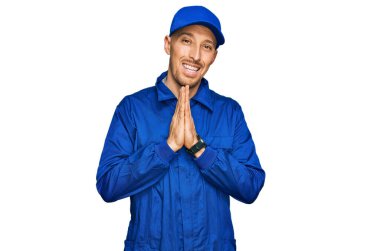 Kel, sakallı, işçi tulumu giyen, elleri birarada dua eden, affedilmek isteyen, kendinden emin, gülümseyen bir adam.. 