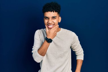 Sıradan kıyafetler giyen genç Afro-Amerikalı adam kameraya kendinden emin bakıyor kollarını kavuşturmuş ve çenesini kaldırmış gülümsüyor. Olumlu düşünmek. 