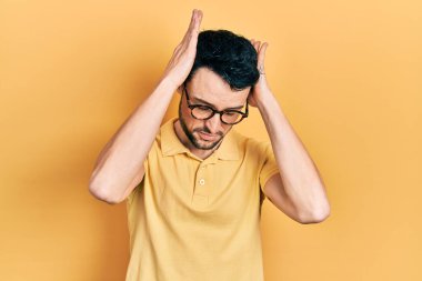 Günlük kıyafetler ve gözlük takan genç İspanyol adam baş ağrısı ve stres yüzünden acı çekiyor çünkü acı ve migren. Eller başının üstünde.. 