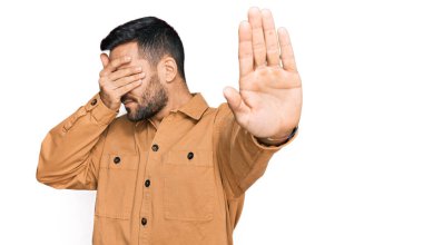 Latin kökenli genç bir adam, günlük kıyafetler giyip, elleriyle gözlerini kapatıyor ve üzgün ve korku ifadeleriyle jestleri durduruyor. utangaç ve olumsuz kavram. 