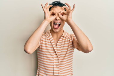 Makyaj yapan yakışıklı bir adam. Günlük tişört giyiyor. Dürbün gibi jest yapıyor. çılgın ifade. 