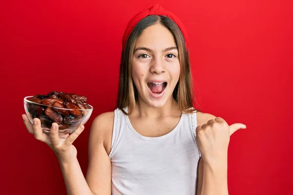 Beautiful Brunette Little Girl Holding Bowl Dates Pointing Thumb Side — ストック写真