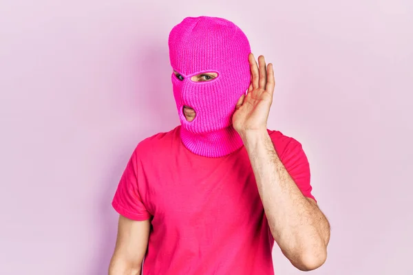身穿粉色巴拉克拉瓦面罩 头戴现代染发的年轻男子面带微笑 两手相对地听着流言或流言蜚语 聋的概念 — 图库照片