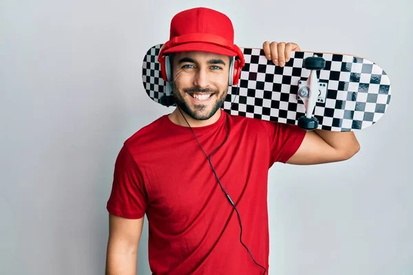 Joven Hombre Hispano Usando Auriculares Sosteniendo Patín Con Aspecto Positivo —  Fotos de Stock