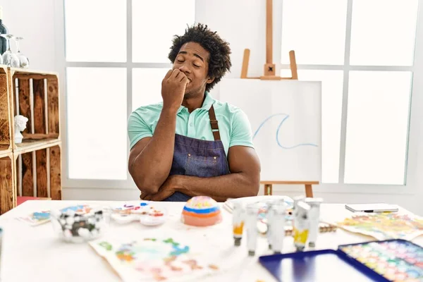 年轻的非洲裔美国人坐在艺术工作室的桌子上 一副紧张而紧张的样子 双手放在咬指甲的嘴上 焦虑问题 — 图库照片