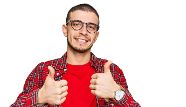 ヒスパニック系の若い男が手で積極的なジェスチャーを行うカジュアル服の成功のサインを着て 親指を笑顔と幸せ 陽気な表情と勝者のジェスチャー — ストック写真