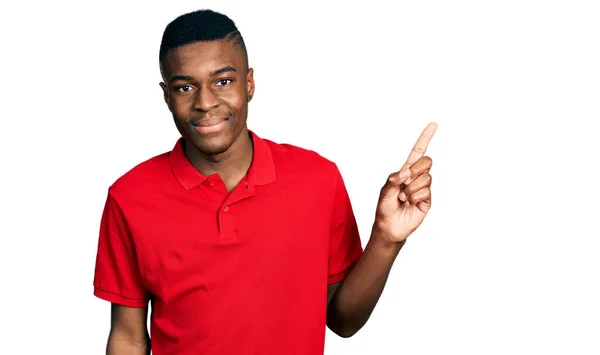 年轻的非洲裔美国人 身穿宽松的红色T恤 脸上挂着大大的笑容 手指头指向侧面看相机 — 图库照片