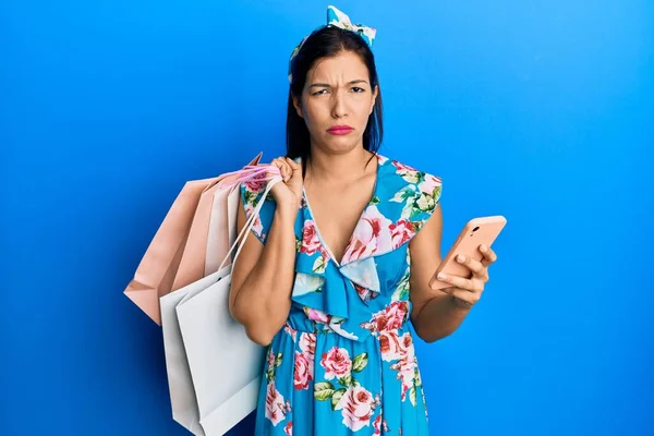 Mladá Latinská Žena Držící Nákupní Tašky Smartphone Skeptická Nervózní Zamračená — Stock fotografie
