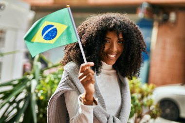 Genç Afrikalı Amerikalı kadın gülümsüyor Brezilya bayrağını şehirde tutarken.