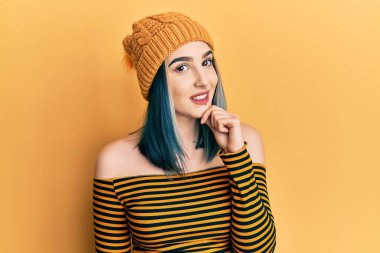 Genç modern kız yün şapka takıyor kameraya özgüvenli bakıyor kolları çapraz ve çenesi açık gülümsüyor. Olumlu düşünmek. 