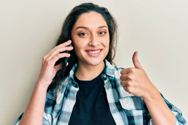 Ortadoğulu güzel bir kadın akıllı telefonla konuşuyor mutlu ve olumlu gülümsüyor, başparmağını kaldırıyor ve onaylıyor. 