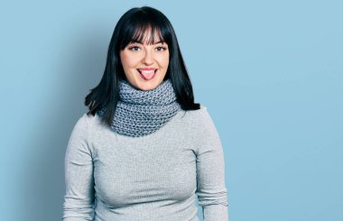 Latin kökenli genç ve kışın atkı takan bir kadın komik bir ifadeyle dilini dışarı çıkartıyor. duygu kavramı. 